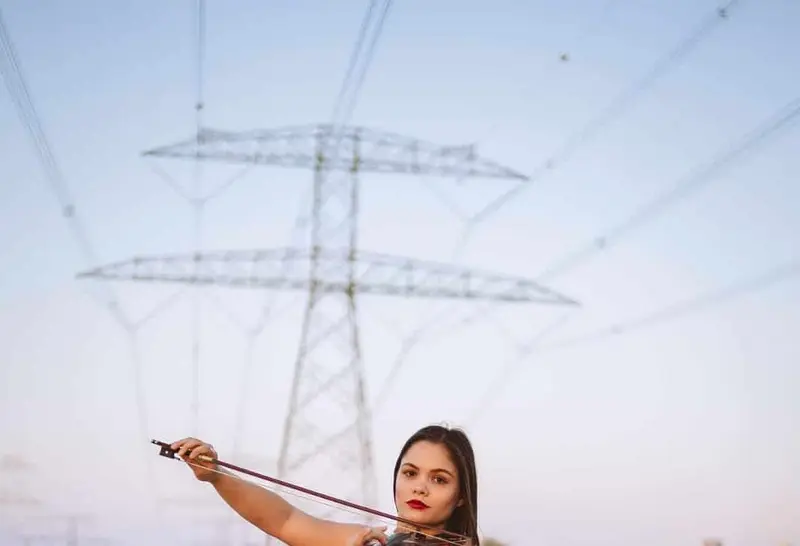 Female violinist in a red gown playing violin on desert sand