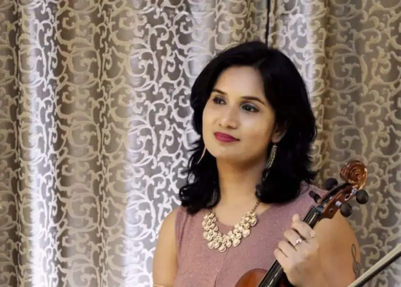 Female violinist in a rose-coloured dress holding a violin, indoor portrait
