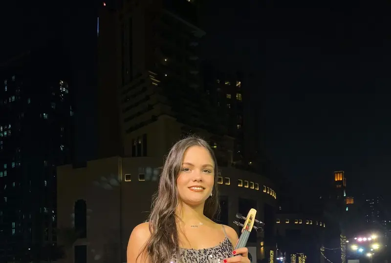 Female violinist in a sequinned gown holding an electric violin at an outdoor evening event
