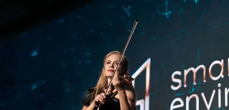 Female violinist performing on stage at a corporate awards evening with a large screen behind