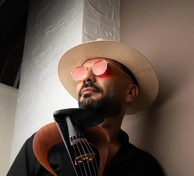 Male violinist in a hat and sunglasses holding a black electric violin