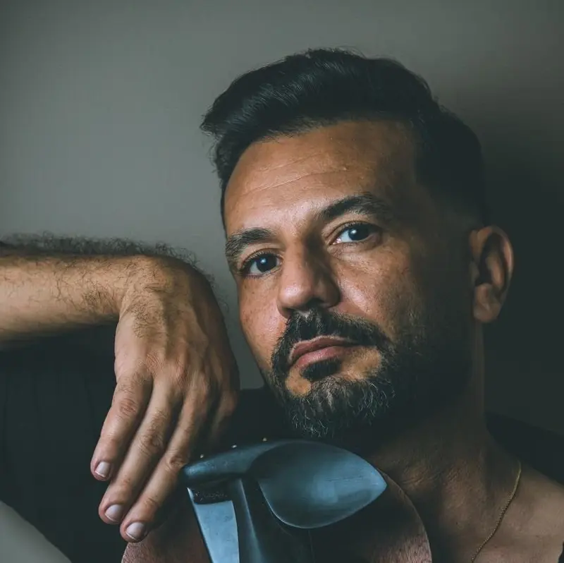 Male violinist resting his chin on his hand above a blue electric violin