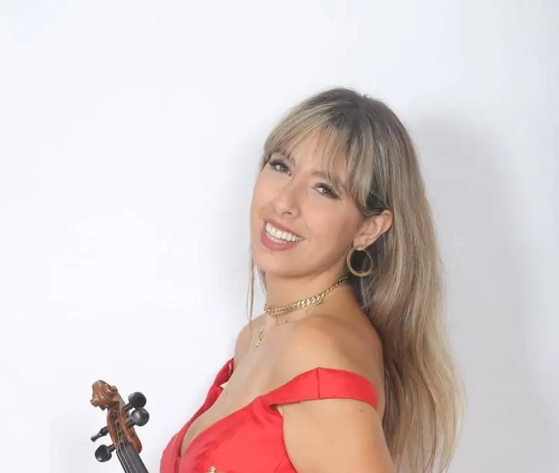 Smiling female violinist in a red off-shoulder dress with her violin, studio portrait